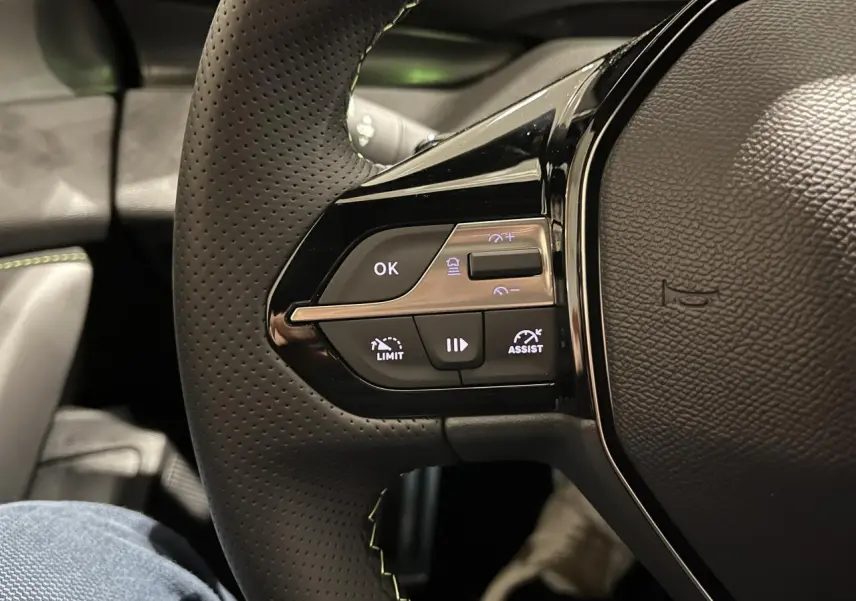 Gros plan sur le volant cuir perforé avec commandes multifonctions et surpiqûres vertes de la Peugeot 308 GT 2024.