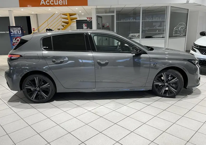 Profil côté gauche d'une Peugeot 308 gris sélénium 2024 en berline GT avec jantes alliage noires en showroom.