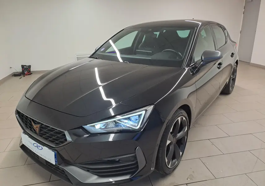 Vue 3/4 avant droite d'une CUPRA Leon 2023 en peinture métallisée Noir Minuit avec phares LED allumés.