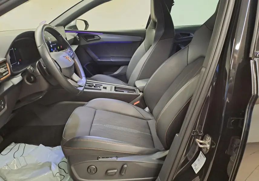 Intérieur avant droit de la CUPRA Leon 2023 noir minuit, sièges sport en cuir avec surpiqûres contrastées et éclairage d’ambiance violet.