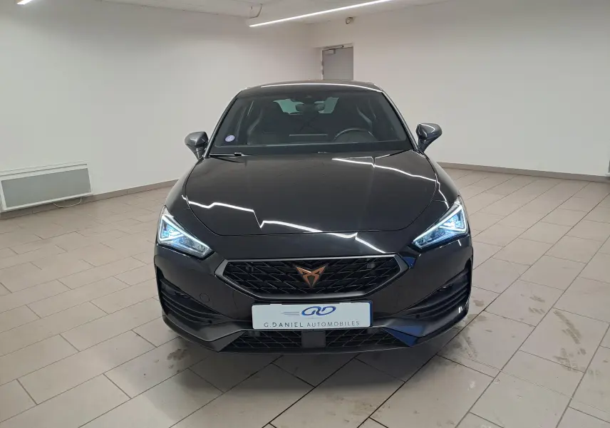 Vue avant d'une CUPRA Leon 1.5 TSI 150 DS7 V noire Minuit avec phares LED allumés dans un showroom.