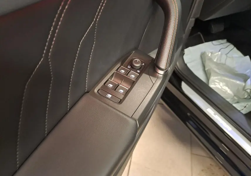 Détail intérieur côté gauche de la porte avec commandes des vitres et surpiqûres orange, seuil de porte Cupra visible sur Leon noir.
