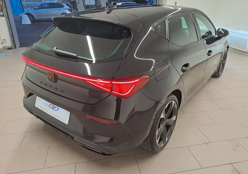 Vue 3/4 arrière droite d'une CUPRA Leon 2023 noir minuit avec feux arrière reliés par un bandeau lumineux LED.