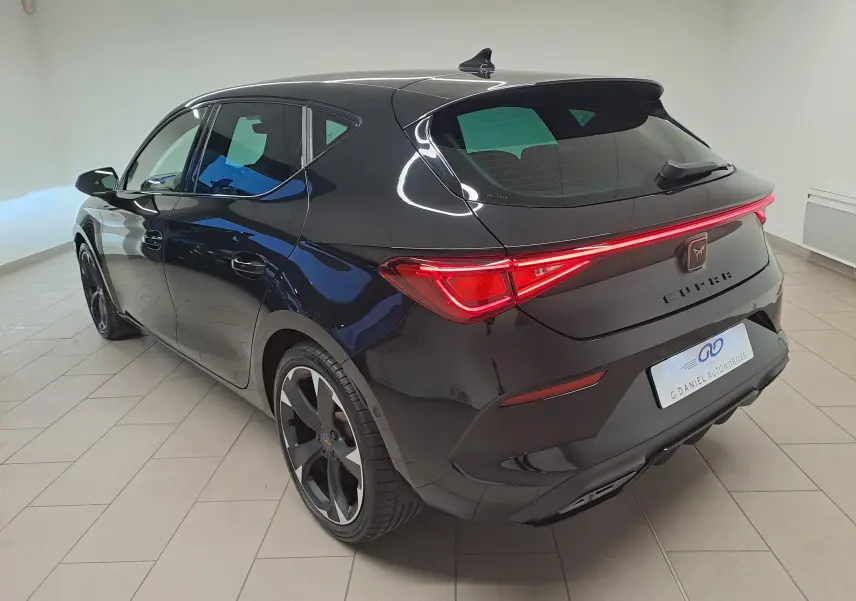 Vue 3/4 arrière droite d'une CUPRA Leon 2023 en noir minuit métallisé avec feux arrière LED et jantes noires distinctives.