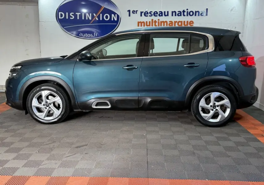 Profil côté gauche d'un Citroën C5 Aircross bleu 2021 en intérieur, avec jantes alliage et barres de toit noires.