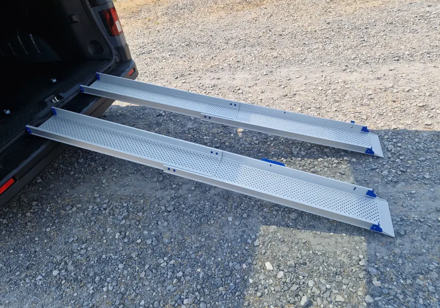 Vue arrière du Renault Trafic Combi noir avec ses rampes d'accès amovibles en aluminium déployées sur un sol gravillonné.