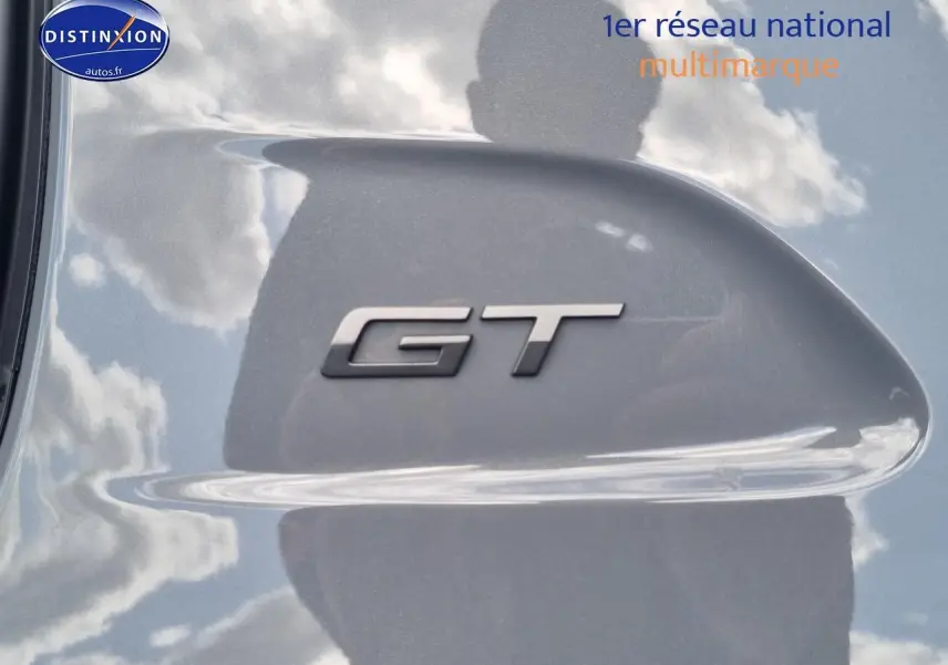 Gros plan sur l’inscription GT en relief sur la carrosserie grise métallisée d’une Peugeot 208 1.2 hybrid 136 GT.
