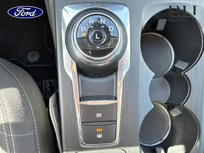 Gros plan sur la molette de sélection de vitesse et les porte-gobelets du Ford Kuga gris, intérieur avec tissu noir rayé.