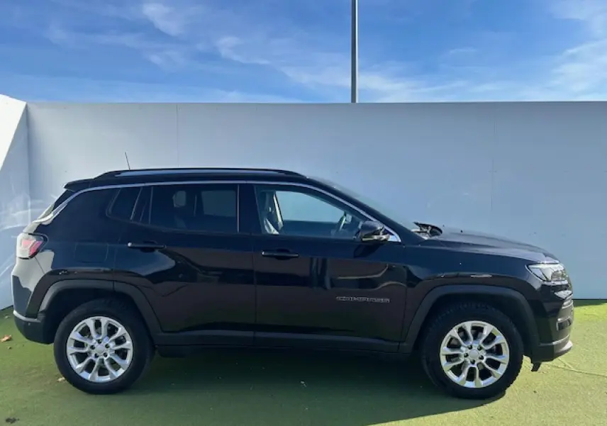 Profil latéral droit d'un Jeep Compass noir métallisé avec jantes alliage et barres de toit longitudinales visibles.