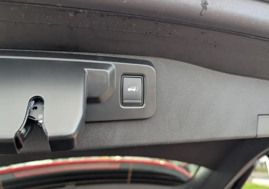 Bouton d'ouverture du hayon électrique sur la face intérieure du coffre d'un Renault Austral rouge métallisé.