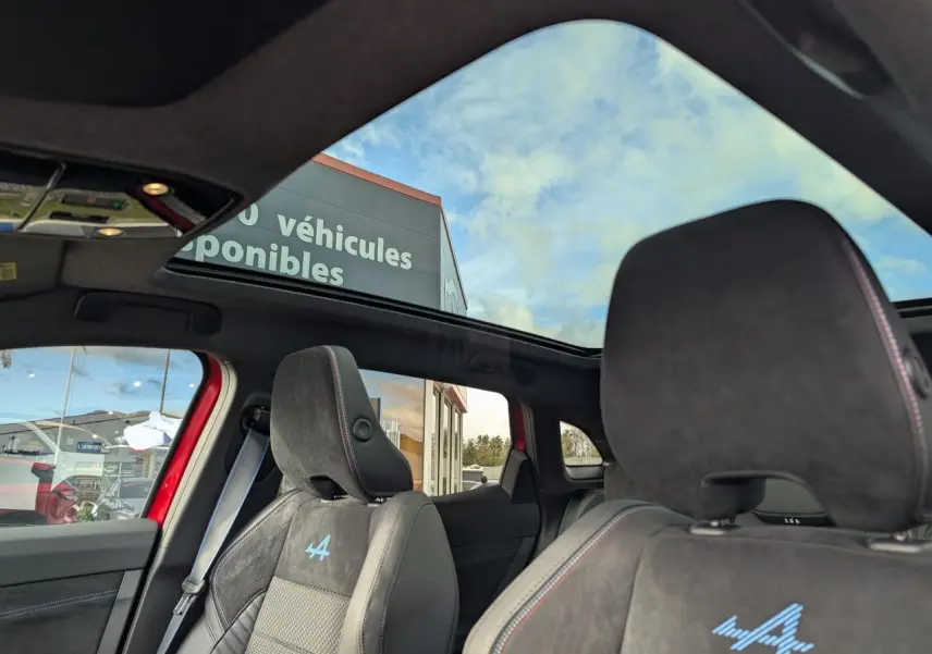 Vue intérieure du toit panoramique et des sièges avant en Alcantara noir avec logo Alpine bleu sur un Renault Austral rouge métallisé.