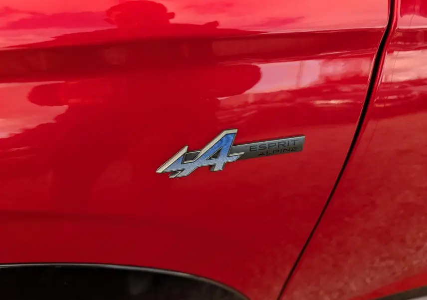Gros plan sur l'écusson Esprit Alpine bleu et noir sur la porte rouge métallisée d'un Renault Austral 2025