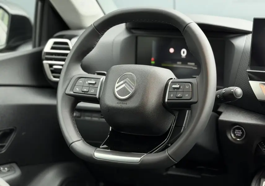 Volant cuir noir de Citroën C4 2025 vu de face, avec commandes intégrées et tableau de bord numérique en arrière-plan.
