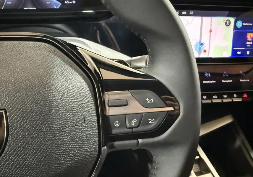 Gros plan sur le volant cuir multifonctions de la Peugeot 308 rouge, avec écran tactile et commandes intégrées visibles.