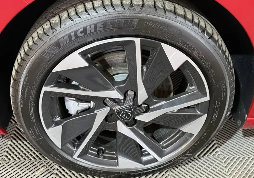 Gros plan sur la jante noire et argentée de la Peugeot 308 rouge, mettant en valeur le logo central et le pneu Michelin.