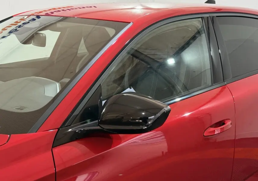 Vue rapprochée du côté gauche avant de la Peugeot 308 rouge, avec rétroviseur noir brillant et poignée de porte intégrée.