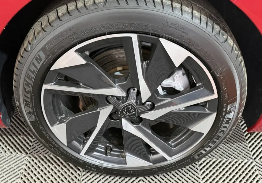 Gros plan sur la jante alliage bicolore d’une Peugeot 308 rouge, mettant en valeur le pneu Michelin et le logo central.