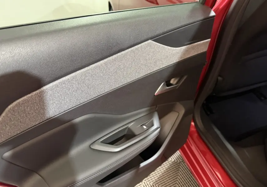 Vue intérieure côté gauche de la porte arrière rouge de la Peugeot 308 BlueHDi 130 AUTO8 ALLURE avec garniture tissu et plastique noir.