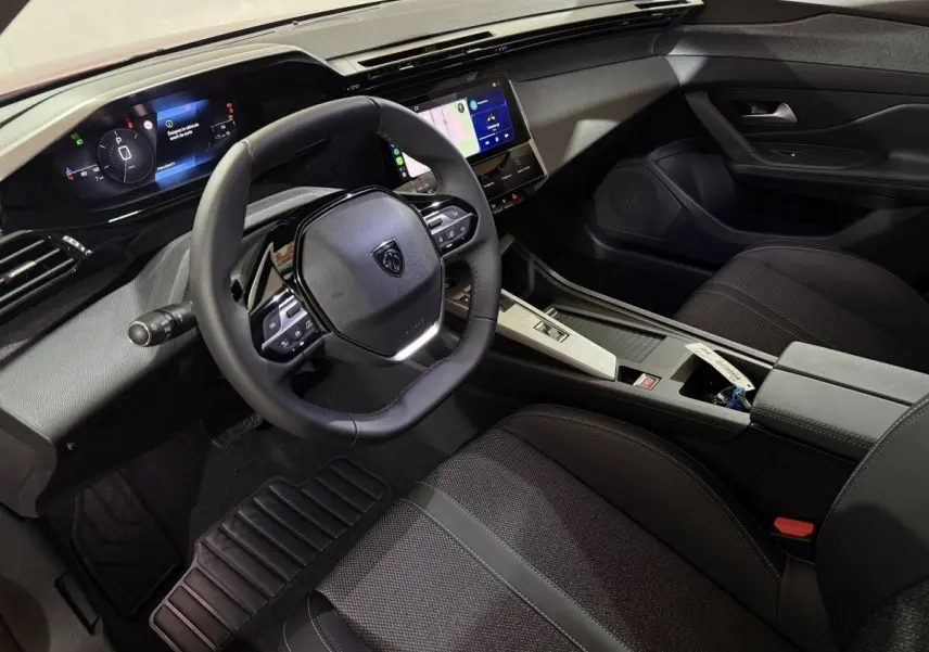 Vue intérieure côté conducteur de la Peugeot 308 2025 avec volant cuir multifonctions et écran tactile central.