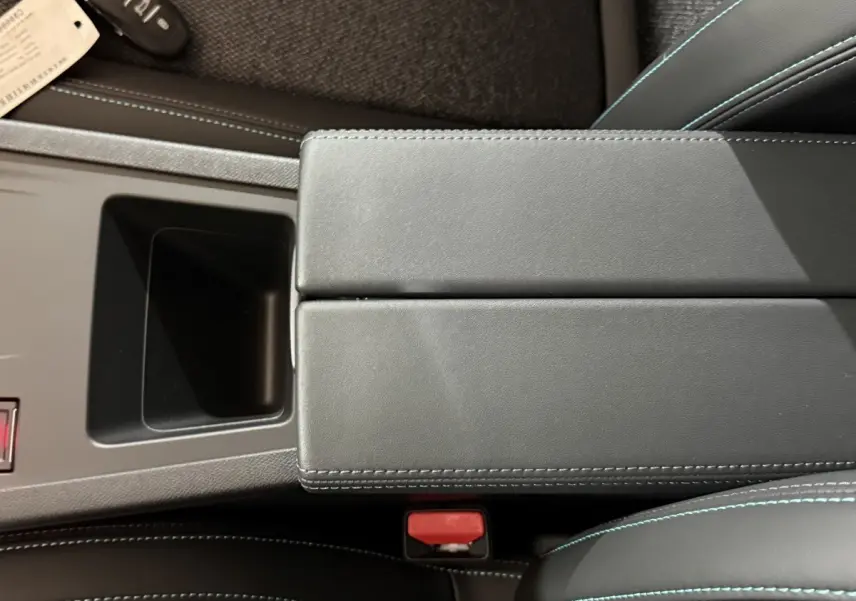 Vue rapprochée de l'accoudoir central noir avec surpiqûres bleues dans l'habitacle de la Peugeot 308 rouge 2025.