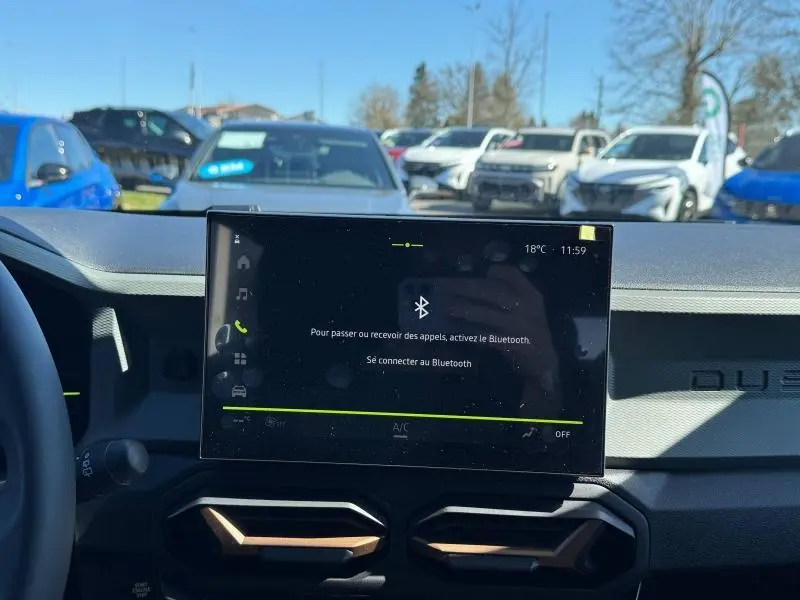 Vue intérieure du tableau de bord du Dacia Duster blanc 2025, avec écran tactile central affichant le Bluetooth.