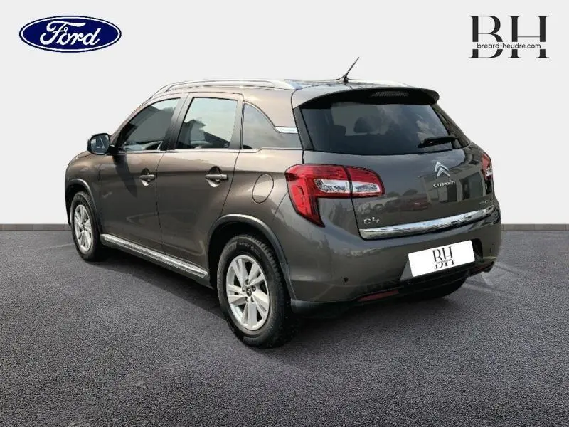 Vue 3/4 arrière droite d'un Citroën C4 Aircross brun Mangaro avec barres de toit et lunette arrière surteintée.