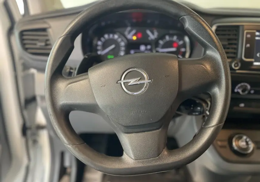 Volant noir avec logo Opel en gros plan, tableau de bord et partie de la planche de bord du Vivaro blanc visible en arrière-plan.