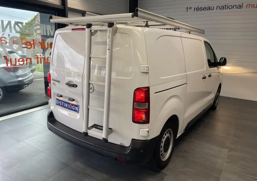 Vue 3/4 arrière droite d'un Opel Vivaro blanc avec échelle et galerie de toit dans un showroom.