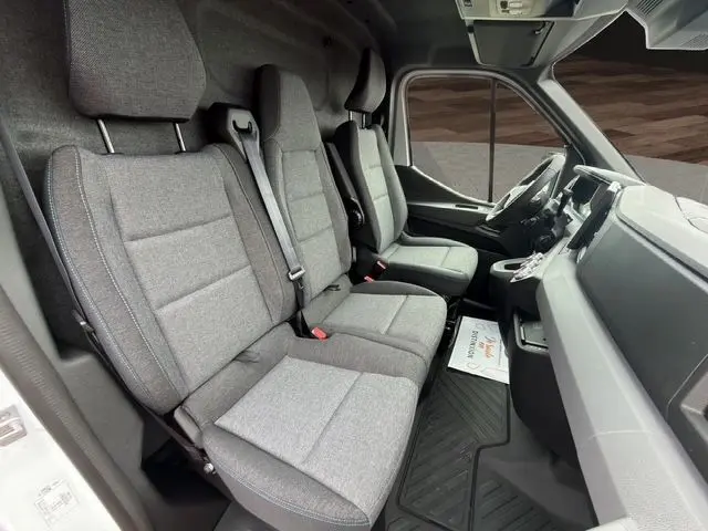 Vue intérieure côté conducteur du Renault Master blanc 2025, montrant la banquette passager grise avec surpiqûres bleues et tableau de bord.