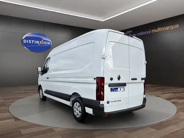 Vue 3/4 arrière droite d’un utilitaire Renault Master blanc avec portes arrière tôlées et logo noir sur fond gris showroom.