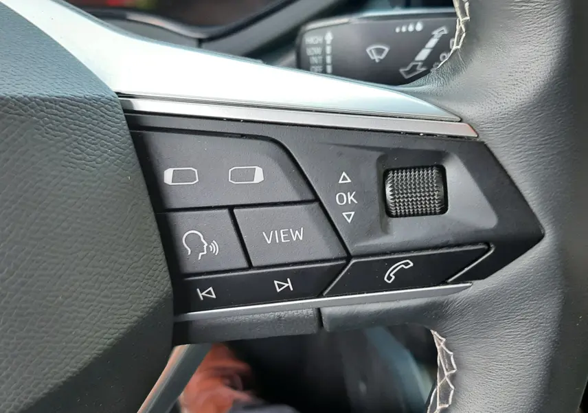 Gros plan sur les commandes au volant noir avec surpiqûres blanches du SEAT Arona 2025, affichage numérique en arrière-plan.