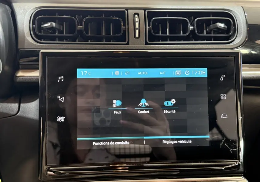 Vue rapprochée de l'écran tactile central noir du tableau de bord de la Citroën C3 blanche, affichant les réglages de conduite.