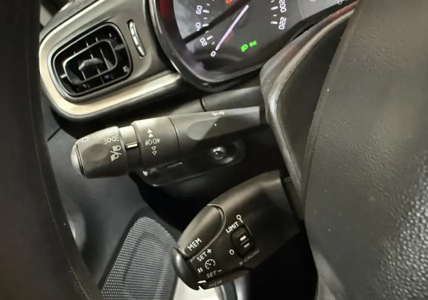 Gros plan sur la colonne de direction et commandes au volant d'une Citroën C3 blanche, tableau de bord partiellement visible.