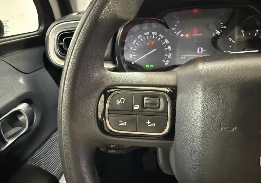 Gros plan sur le volant noir de la Citroën C3 2021 avec commandes intégrées et tableau de bord lumineux en arrière-plan.