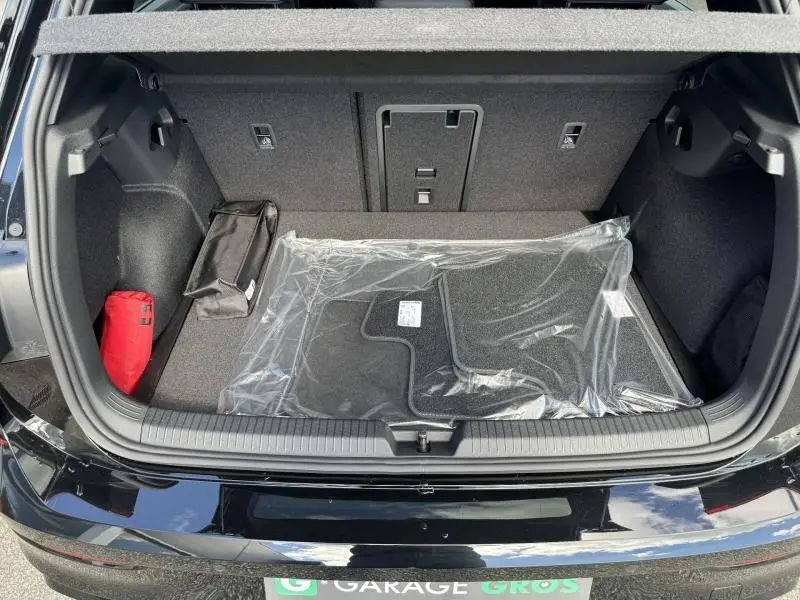 Coffre ouvert d’une Volkswagen Golf gris lunaire, vue de l’arrière, tapis de sol neufs et trousse de secours visibles.