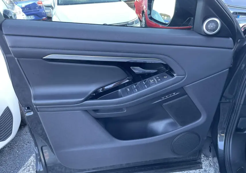 Gros plan sur la porte avant droite noire du Range Rover Evoque avec commandes électriques et haut-parleur intégré.