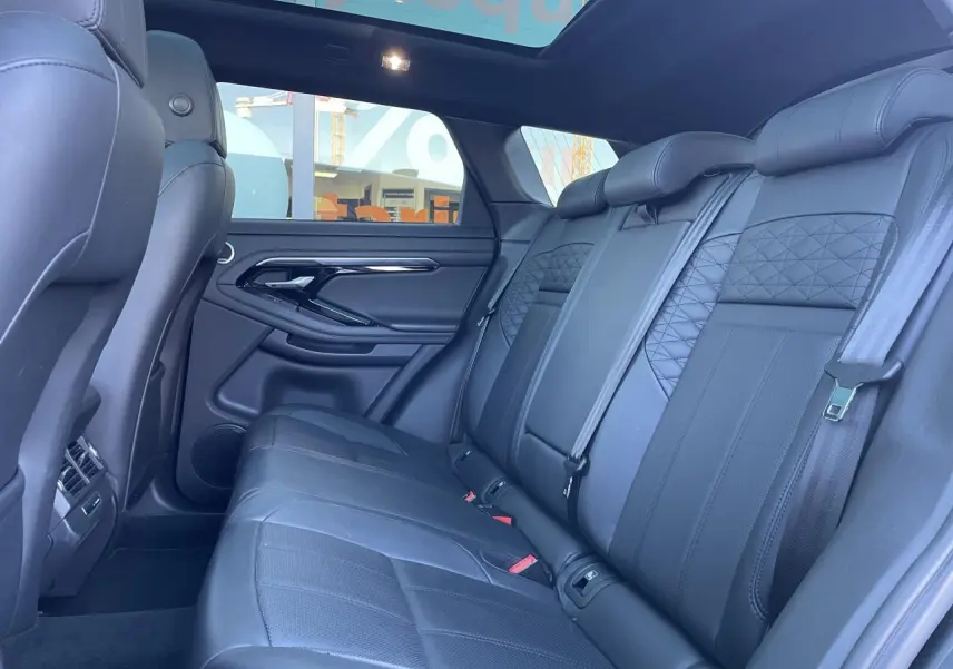 Vue latérale intérieure du Range Rover Evoque 2019 montrant les sièges arrière en cuir noir et le toit panoramique.