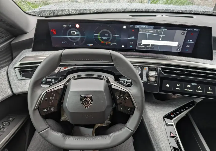 Vue intérieure du volant compact cuir et du tableau de bord numérique panoramique du Peugeot 5008 Gris Artense 2025 Allure hybride.