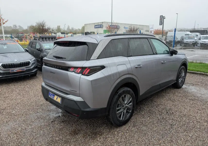 Vue 3/4 arrière droite d'un Peugeot 5008 gris Artense avec feux arrière à LED et jantes alliage 18 pouces sur parking humide.