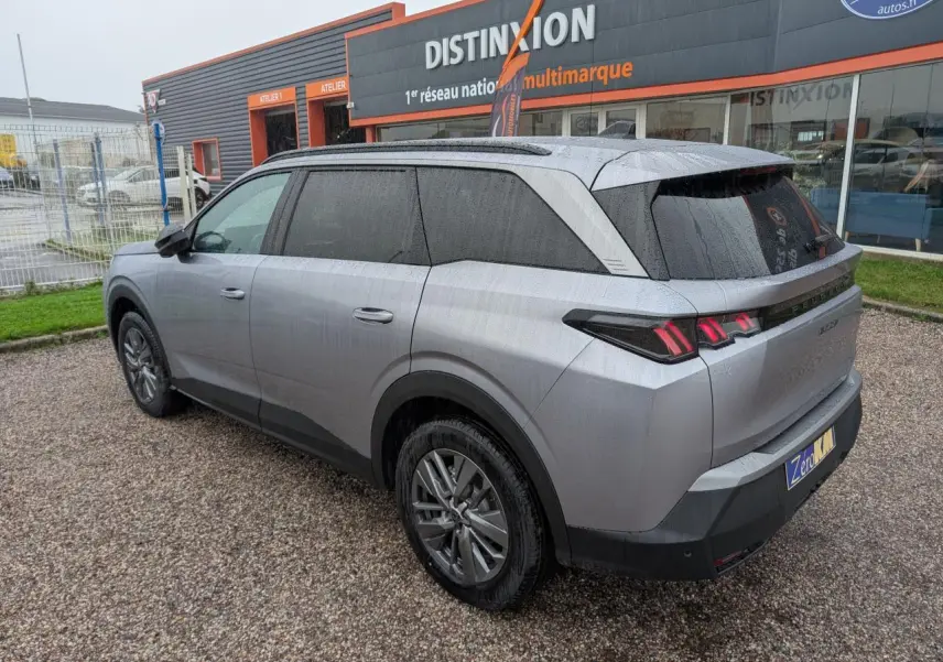 Peugeot 5008 gris Artense vue 3/4 arrière droit sous la pluie avec feux arrière à LED 3 griffes allumés.