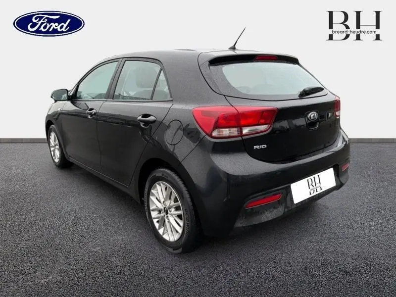 Vue 3/4 arrière droite d'une KIA Rio noire Ébène avec jantes alu et feux arrière distinctifs.