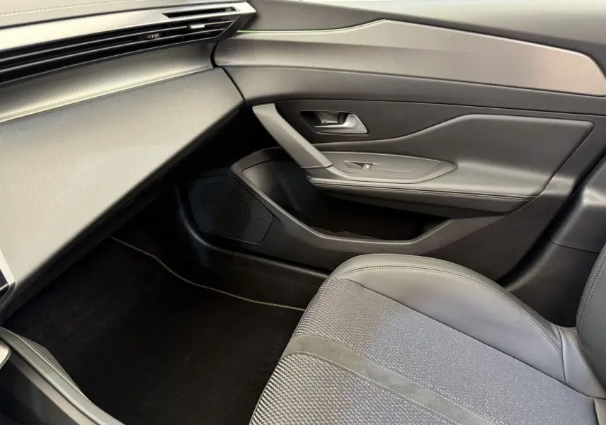 Vue intérieure côté passager avant de la Peugeot 308 Hybrid 136 e-DCS6 GT avec sellerie grise et garnitures noires.