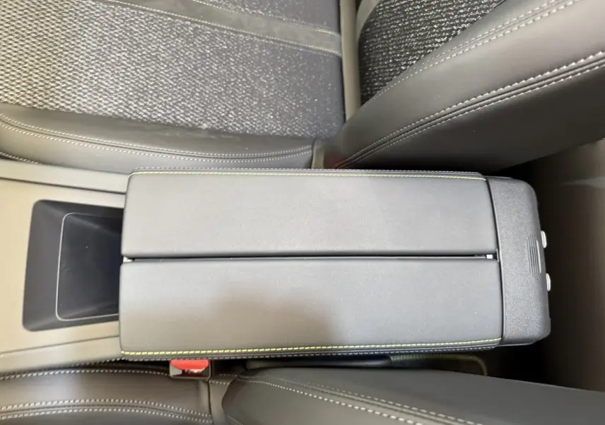 Gros plan sur l'accoudoir central en cuir noir avec surpiqûres vertes, entre les sièges avant gris foncé du Peugeot 308 Hybrid 2024.