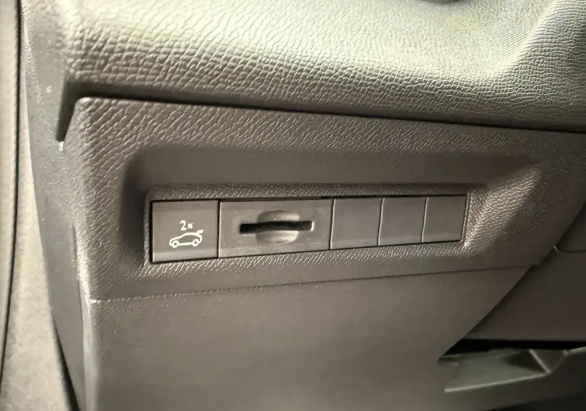 Gros plan sur le bouton d'ouverture du coffre dans l'habitacle d'une Peugeot 308 Hybrid gris foncé.