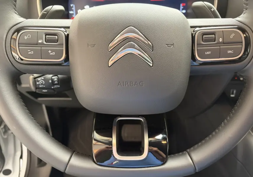 Gros plan sur le volant noir du Citroën C5 Aircross 2025 avec commandes multifonctions et logo chromé central.