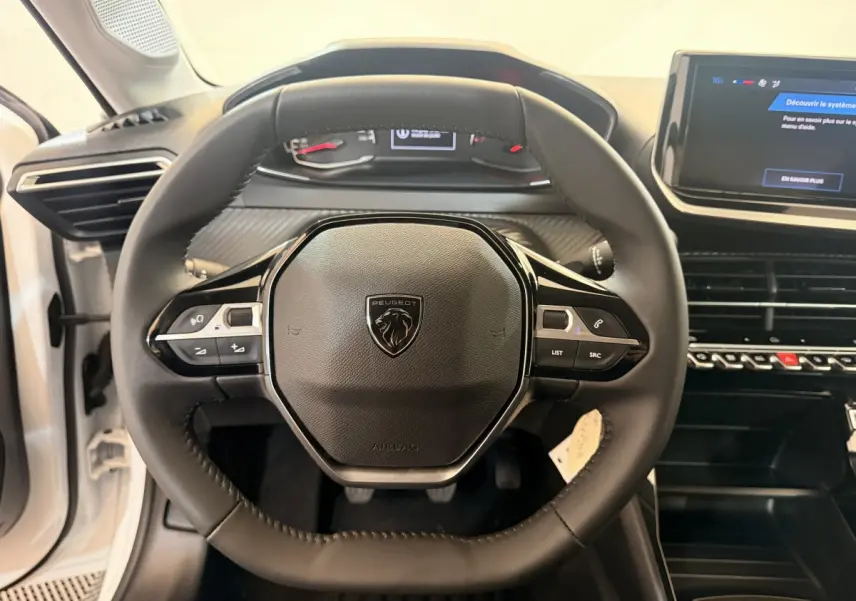 Vue rapprochée du volant cuir noir de la Peugeot 208 blanche, avec tableau de bord digital et écran tactile central.