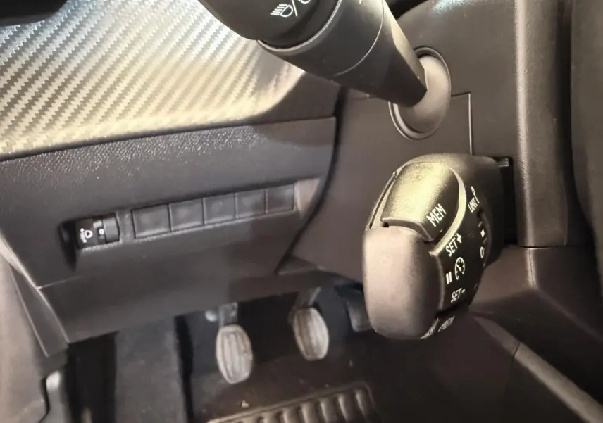 Gros plan sur la commande de régulateur de vitesse et les pédales côté conducteur d'une Peugeot 208 essence blanche.