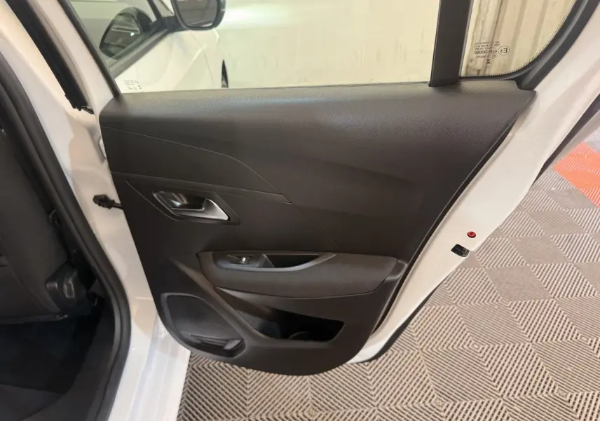 Vue rapprochée de la porte arrière droite ouverte d’une Peugeot 208 blanche, intérieur noir avec poignée et haut-parleur intégrés.