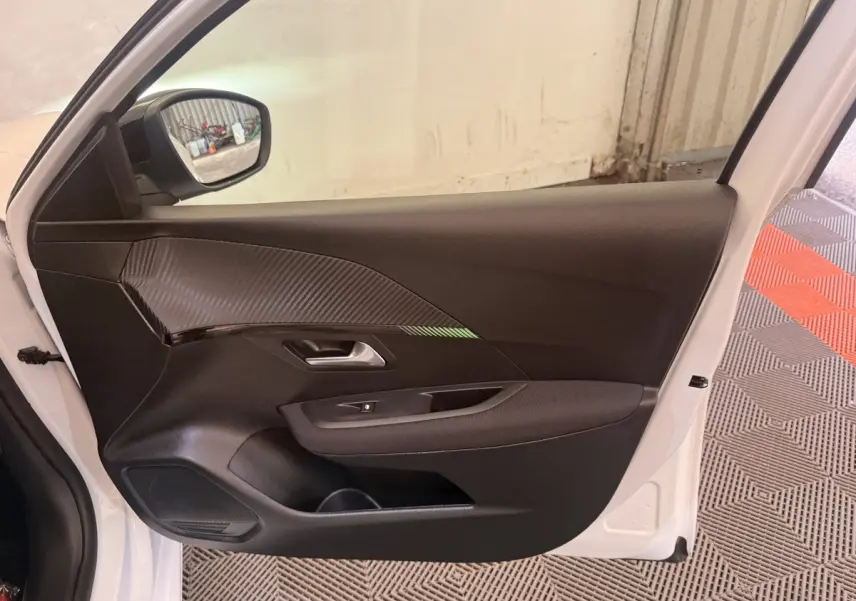 Vue côté gauche de la porte avant blanche d’une Peugeot 208 2025 avec garniture noire et insert effet carbone.