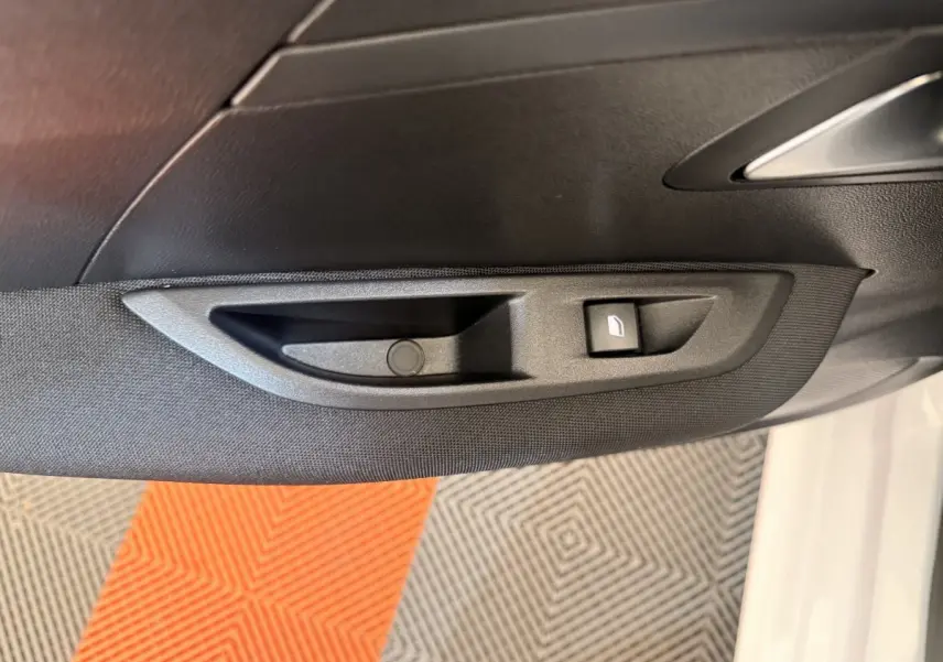 Poignée intérieure côté gauche avec bouton de lève-vitre sur porte d’une Peugeot 208 blanche vue de près.